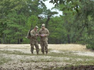 two u.s. soldiers standing in the woods, one wearing a backpack with a large antenna array and a handset